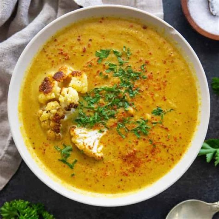 Cauliflower soup in red and grey bowls topped with white cheddar.