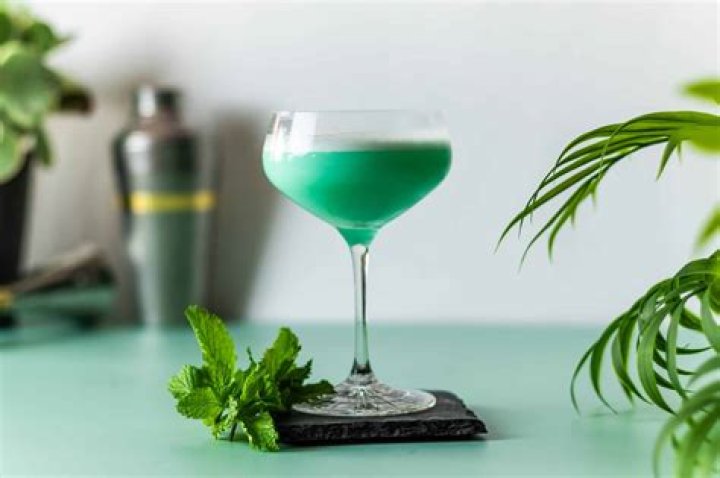Green grasshopper drink in a stemmed glass with swirled with chocolate syrup.