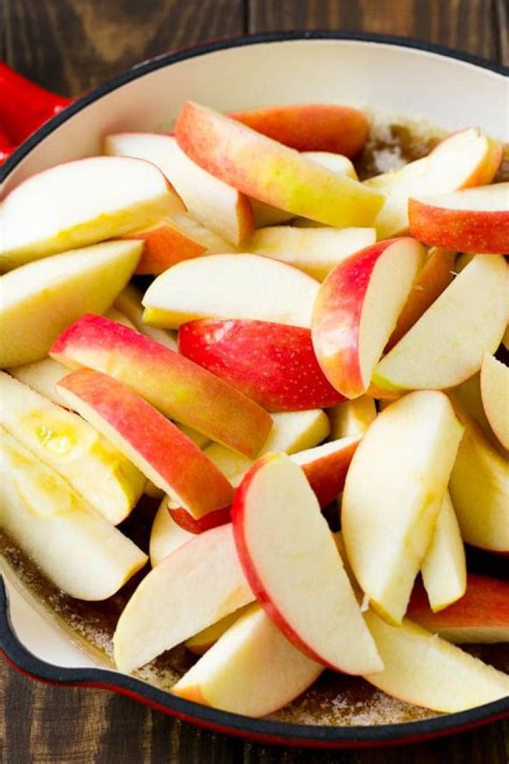 Sliced apples in a pan with syrup and cinnamon being poured over the top.